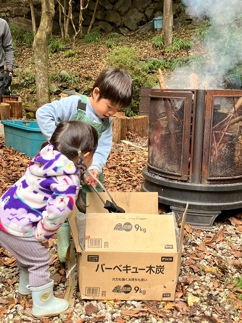 焚き火体験で焚火に炭を入れる子どもの写真